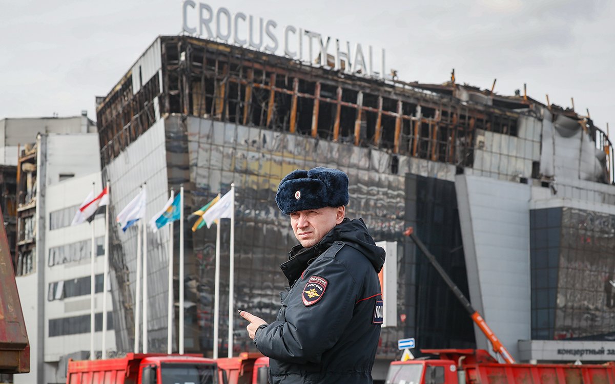 Сотрудник полиции патрулирует территорию перед сгоревшим концертным залом «Крокус Сити Холл», когда скорбящие собираются у мемориала жертвам, через четыре дня после теракта в Красногорске, Подмосковье, Россия, 26 марта 2024 года. Фото: Юрий Кочетков / EPA-EFE